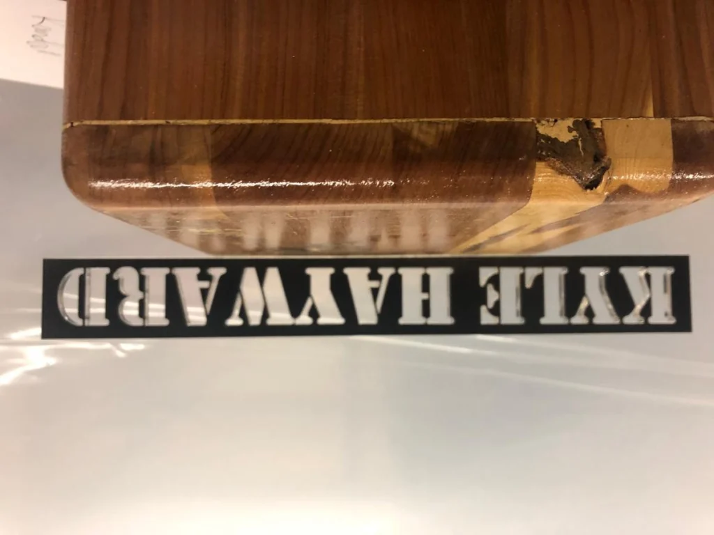 Engraved wooden sign on surface, reads 'Kyle Hayward'.